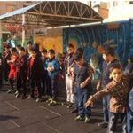 گروهی از دانش‌آموزان در صف ایستاده در حیاط مدرسه تحت سایبان