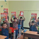 دانش‌آموزان در کلاس درس در حال نمایش کتاب‌های قرمز رنگ در جریان یک فعالیت یا رویداد کتاب