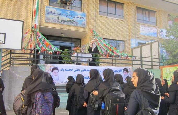 دختران دانش‌آموز در حیاط مدرسه در حال شرکت در یک مراسم و رویداد دسته‌جمعی با تابلوهای رنگی و بنرهای تزیینی