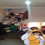 دانش‌آموزان در حال شرکت در فعالیت جمعی درون کلاس درس مدرسه، با دیوار‌های رنگی و تزئینات بخش آموزشی