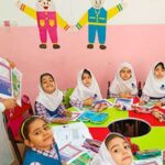 دانش‌آموزانی در حال انجام فعالیت مطالعه و خواندن کتاب‌های رنگی در کلاس درس تحت نظارت معلم