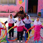 دانش‌آموزان دختر در حیاط مدرسه در حال انجام فعالیت گروهی با طناب‌های رنگی تحت نظارت معلم