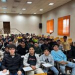 دسته بزرگی از دانش‌آموزان در یک کلاس درسی به هنگام برگزاری یک مراسم یا رویداد، برخی نشسته و برخی ایستاده