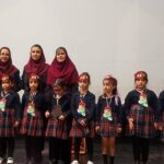 گروهی از دانش‌آموزان و معلمان با لباس یکدست و تاج‌های تزئینی در حین یک مراسم یا رویداد مدرسه‌ای