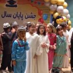 دانش‌آموزان در حال حضور در مراسم جشن پایان سال تحصیلی با لباس‌های مختلف و رنگین، با بنر و تزیینات در پس‌زمینه