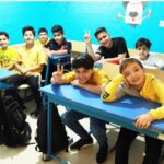 دانش‌آموزان در حال انجام فعالیت رباتیک و STEM در کلاس درس با میزهای آبی، کنترل دستگاه پرنده‌ای