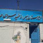 درب و سردر ورودی دیرستان با تابلوی آبی و درب‌های فیروزه‌ای رنگ