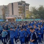 تجمع بزرگ دانش‌آموزان با لباس‌های آبی یکسان در حیاط مدرسه در حال برگزاری یک فعالیت یا مراسم گروهی