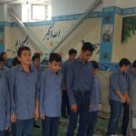 تصویر گروهی از دانش‌آموزان پسر مدرسه ایستاده در حیاط، لباس یکسان آبی رنگ، حین برگزاری تجمع یا مراسم