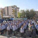 صبحگاه دانش‌آموزان و پرسنل مدرسه در حیاط مدرسه، تجمع دستهای منظم دانش‌آموزان با لباس مدرسه و معلمان در فضای باز