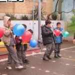 دانش‌آموزان در حیاط مدرسه در حال شرکت در مراسم با بالون‌های رنگی و فعالیت‌های گروهی