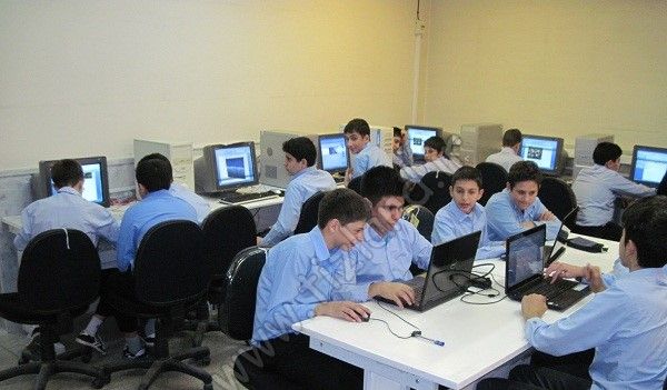دانش‌آموزان پسر با لباس مدرسه در حال کار روی کامپیوترها (لپ‌تاپ و دسک‌تاپ) در سایت کامپیوتر مدرسه