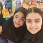 گروه دانش‌آموزان دختر با لباس مدرسه در حال خندیدن و لذت بردن از لحظه‌ای اجتماعی در محیط رنگین مدرسه