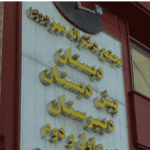 نمای بیرونی ساختمان‌های مدرسه با درب ورودی و تابلوی نام فارسی