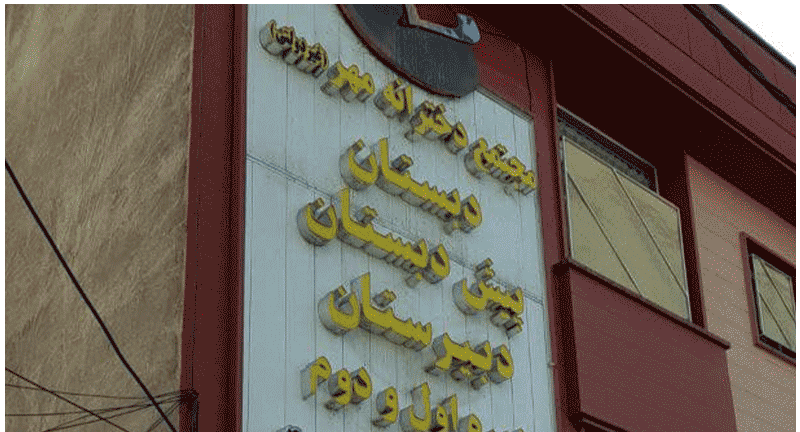 نمای بیرونی ساختمان‌های مدرسه با درب ورودی و تابلوی نام فارسی