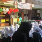 دانش‌آموزان دختر مدرسه در حیاط ایستاده‌اند و یک مراسم یا جشن‌واره با تزیینات رنگی و بادکنک‌ها برگزار می‌شود