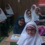 دانش‌آموزان دختر در کلاس درس نشسته‌اند و کتاب‌های مرجع را با هم مطالعه می‌کنند
