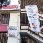 نمای بیرونی ساختمان مدرسه با تابلوهای اطلاعاتی و سردری آجری
