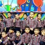 گروهی از دانش‌آموزان در لباس مدرسه‌ای، ایستاده در برابر پس‌زمینه‌ی رنگین با تجهیزات ورزشی