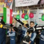 دانش‌آموزان در یک مراسم نمایش پروژه‌های علمی، مدل‌های موشک و پهپاد خود را به‌میان می‌گذارند؛ تزئین با بادکنک‌های رنگی و پرچم ملی
