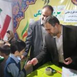 دو مسئول مدرسه در لباس رسمی در حال تعامل و صحبت با دانش‌آموزان در کلاسی با دیوارهای رنگی و فلاگ ایران