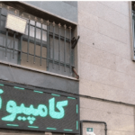 نمای خارجی سردر و دیوار ساختمان مدرسه با پنجره‌های فلزی و تابلوی سبز، عکس در روز روشن