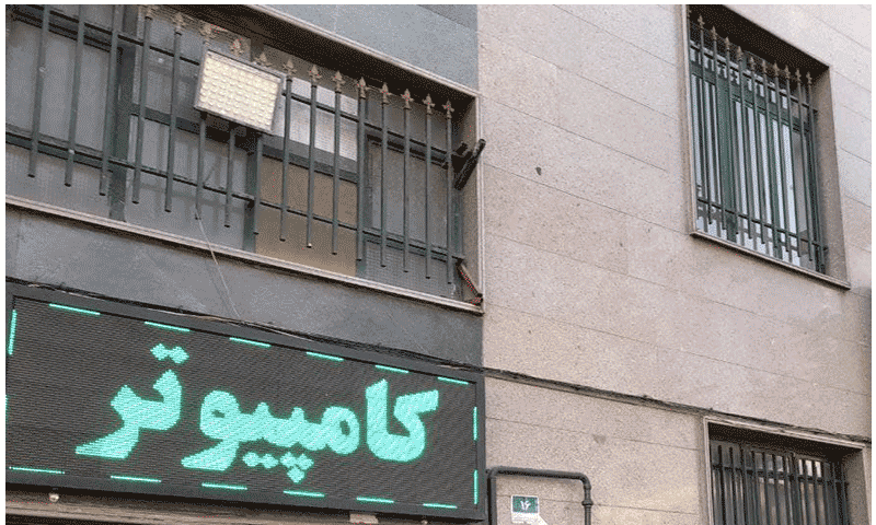 نمای خارجی سردر و دیوار ساختمان مدرسه با پنجره‌های فلزی و تابلوی سبز، عکس در روز روشن