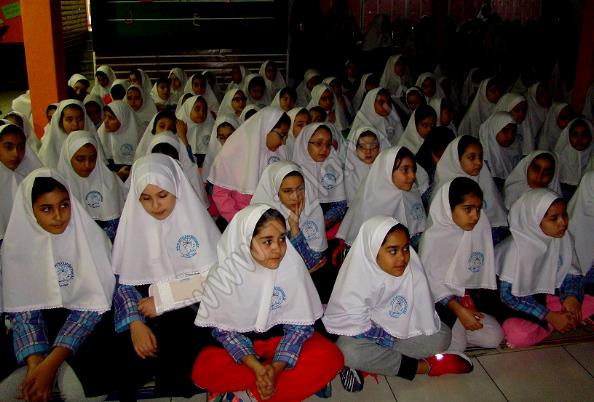دانش‌آموزان با لباس یکسان و حجاب سفید در حال شرکت در یک مراسم یا فعالیت گروهی درون‌سالنی