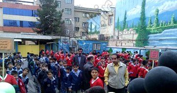 تجمع انبوه دانش‌آموزان در حیاط مدرسه برای شرکت در یک مراسم یا رویداد مدرسه‌ای با پوشش لباس‌های قرمز و آبی