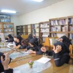 دانش‌آموزان دختر در کتابخانه مدرسه در حال مطالعه و تحصیل در میان قفسه‌های کتاب‌های متنوع