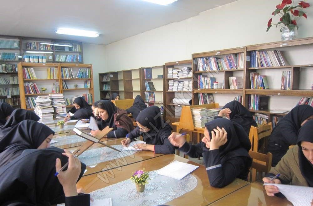 دانش‌آموزان دختر در کتابخانه مدرسه در حال مطالعه و تحصیل در میان قفسه‌های کتاب‌های متنوع