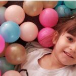 دانش‌آموز خردساله لبخند‌زن در میان توپ‌های بادی رنگی متعدد در حال بازی و سرگرمی