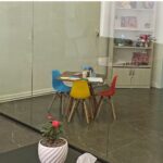 نمای داخلی کلاس درس معاصری با میز تحصیلی سفید، صندلی‌های رنگی، قفسه‌های رشته‌ای، تخته سفید، و تجهیزات یادگیری