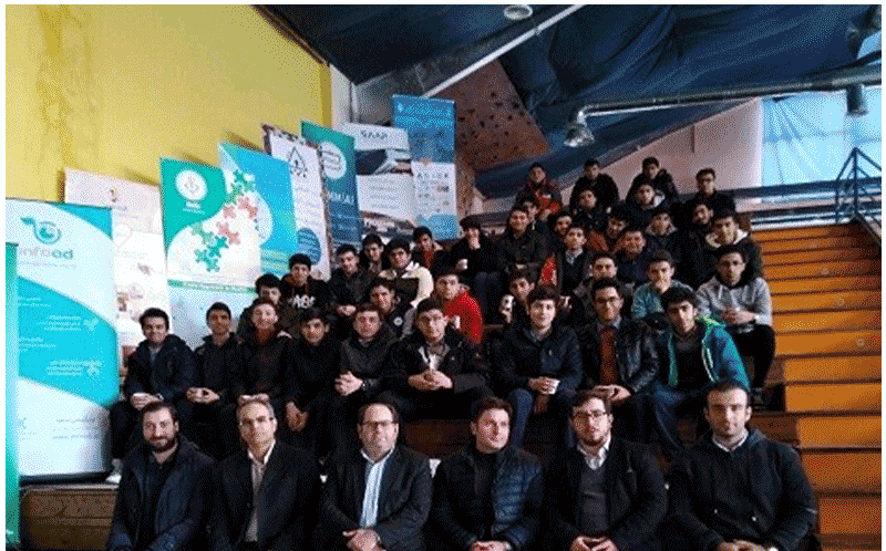 دسته گروهی دانش‌آموزان و معلمان در یک رویداد یا جمع‌آوری مدرسه‌ای، با تابلوهای بنر آبی در پس‌زمینه