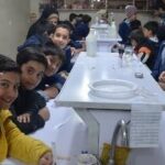 دانش‌آموزان در حال انجام فعالیت عملی و آزمایشی دور یک میز سفید در چارچوب یک رویداد آموزشی سازمان‌یافته