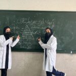 دو دانش‌آموز در حال ارائه و توضیح مطالب علمی با نمودار روی تخته سیاه در کلاس درس