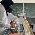 دانش‌آموزی با لباس آزمایشگاهی در حال انجام آزمایش شیمیایی با شیشه‌آلات و تجهیزات آزمایشگاهی