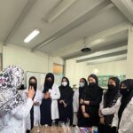 دانش‌آموزان در حال مطالعه و یادگیری گروهی حول یک پوستر آموزشی در کلاس درس، با راهنمایی یک معلم