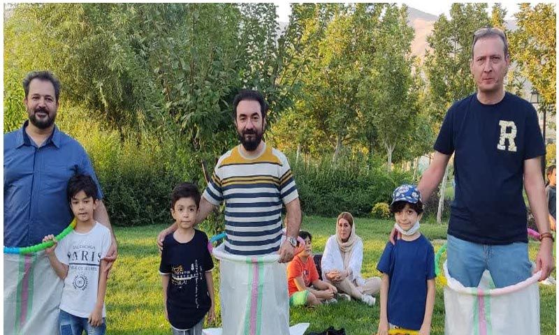 گروهی از معلمان و دانش‌آموزان در حیاط مدرسه در حال شرکت در فعالیت‌های تیمی و آموزشی با درختان سبز در پس‌زمینه
