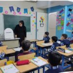 معلم و دانش‌آموزان در کلاس درس با تزئینات رنگی روی دیوار و تابلو سیاه