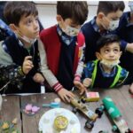 دانش‌آموزان در حال شرکت در یک فعالیت دستی و خلاق با استفاده از مصالح و ابزارهای مختلف بر روی میز