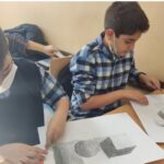 دو دانش‌آموز در حال انجام یک پروژه ترسیم و رسم گرافیتی روی میز درسی