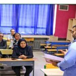 معلم در حال تدریس به دانش‌آموزان در کلاس درس با پنجره‌های آبی و دیوار قرمز