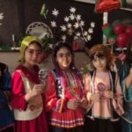 دانش‌آموزان در لباس‌های سنتی رنگین حین جشن نوروز با تزئینات گل‌های سفید و میوه‌های قاچ نوروز در پس‌زمینه