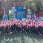 دانش‌آموزان مدرسه نده در یک مراسم جمعی با لباس صورتی ایستاده، پس‌زمینه نصب هنری رنگی