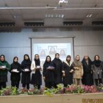 گروهی از دانش‌آموزان زن بر روی صحنۀ یک مراسم رسمی با گل‌های تزیینی و پروجکتور در پس‌زمینه