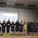 تصویری از مراسمی در سالن با دانش‌آموزان ایستاده روی صحنه و پرده‌نمایش درحال نمایش تصاویر آن‌ها