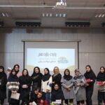 گروهی از دانش‌آموزان در حال ارائه و اجرای پروژه‌ای در سالن مدرسه، با پرتابل روشن و پرده قرمز