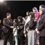 معلم و دانش‌آموزان در یک مراسم و برنامه‌ی ویژه در سالن تاریک مدرسه