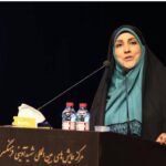 دانش‌آموزی با لباس رسمی در حال سخنرانی روی سن با میکروفن در جلوی تالار تماشاخانه‌ای